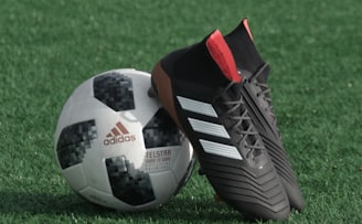 black adidas cleats lean on white and black adidas soccer ball on green grass