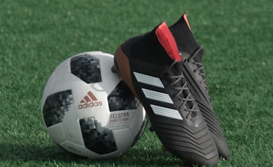 black adidas cleats lean on white and black adidas soccer ball on green grass