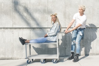 woman sitting on serving cart while man holding push cart