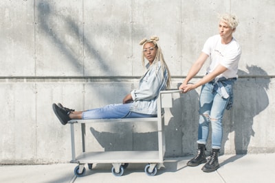 woman sitting on serving cart while man holding push cart