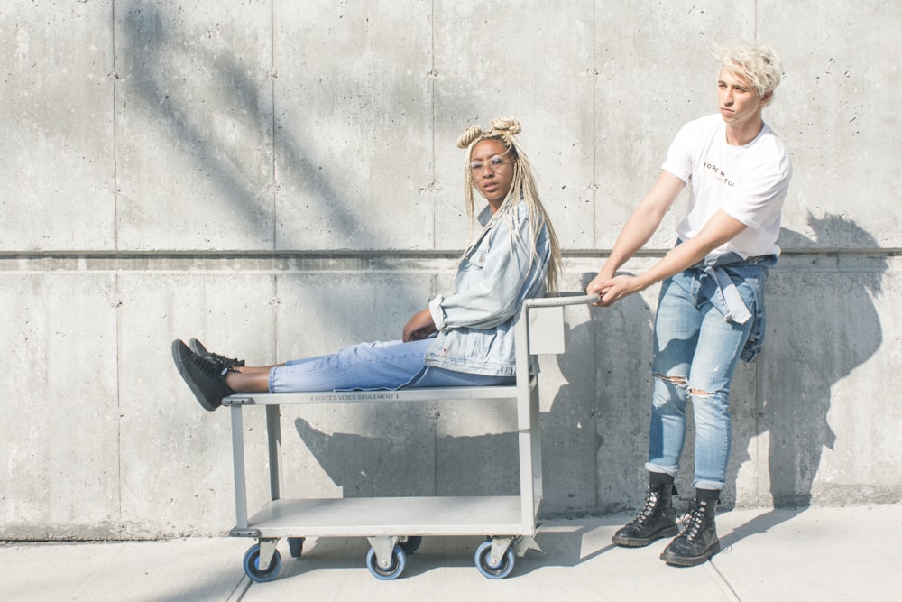 woman sitting on serving cart while man holding push cart