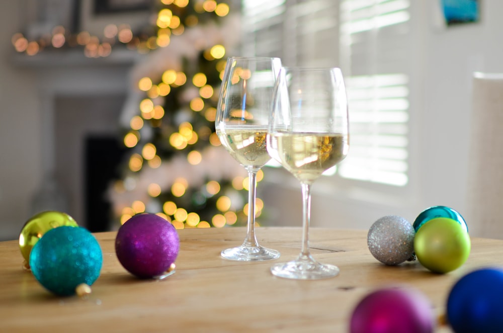 Due bicchieri da vino con piedi chiari riempiti di liquido giallo vicino a ornamenti a sfera di colori assortiti