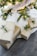Several neatly wrapped gifts are placed under a Christmas tree, decorated with lights, pine cones, and baubles. The presents feature elegant gold and white paper with simple twine and greenery accents.