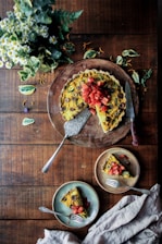 A rustic wooden table displaying a colorful seasonal vegetable tart with fresh herbs.