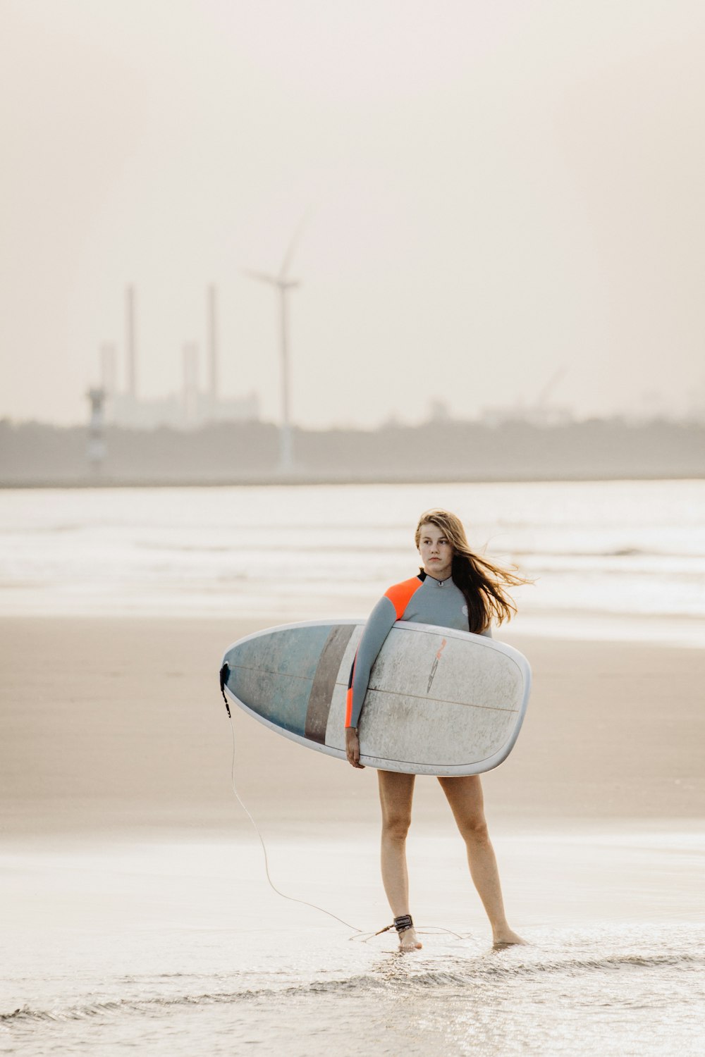 woman standing on seashore carrying surfboard