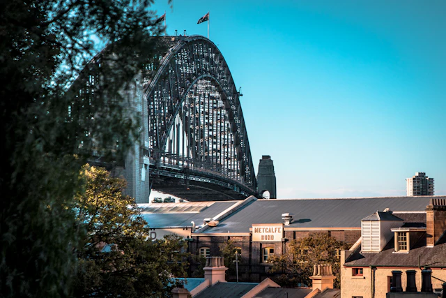 The Sydney Harbour Bridge rises behind the historic sandstone rooftops of The Rocks, including the Metcalfe building.