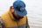 man wearing vest and cap looking down beside body of water
