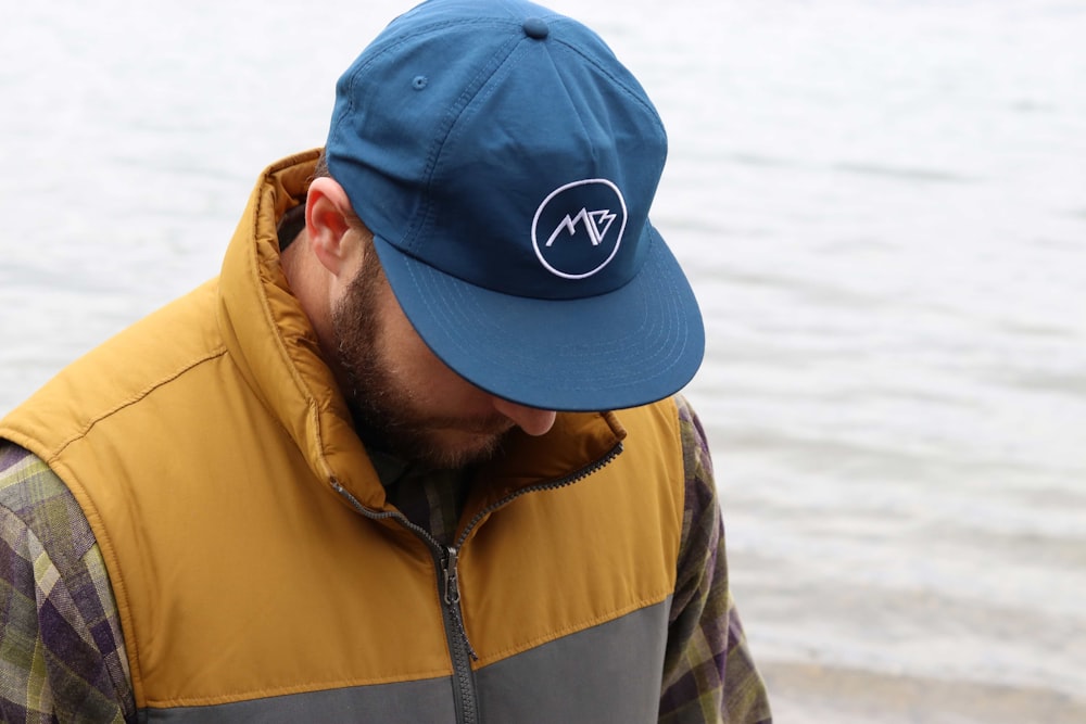 man wearing vest and cap looking down beside body of water