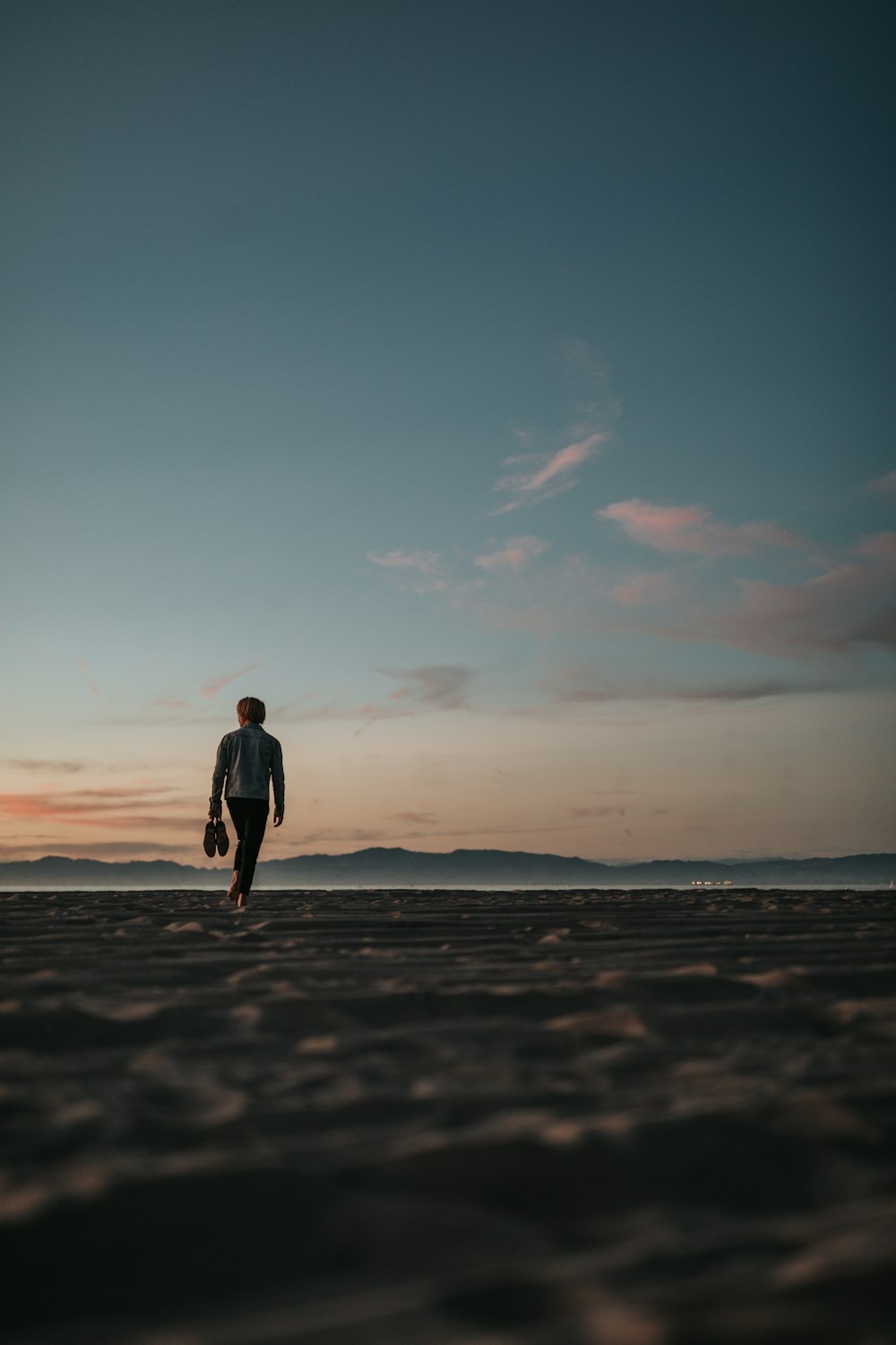 man walking on sand while holding his footwears