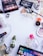 A collection of various makeup and skincare products arranged on a white surface. The items include eyeshadow palettes, false eyelashes, brushes, lipsticks, foundation, eyelash curler, and other cosmetics. There are also decorative white flowers scattered around the products.