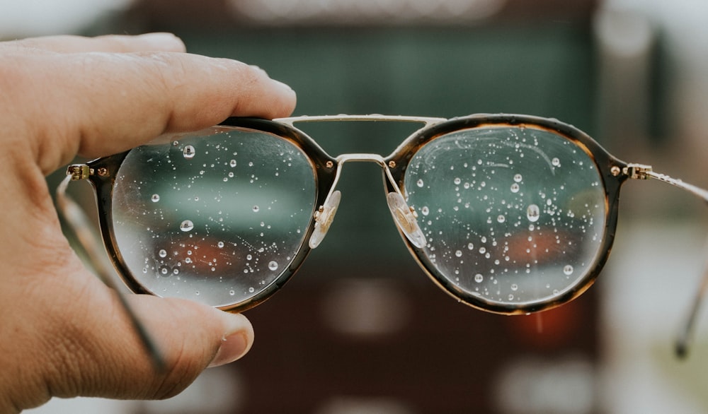 a hand holding a pair of glasses with water droplets on it