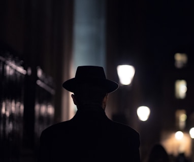 man in black hat walking on sidewalk during night time