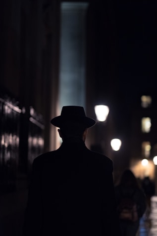 man in black hat walking on sidewalk during night time