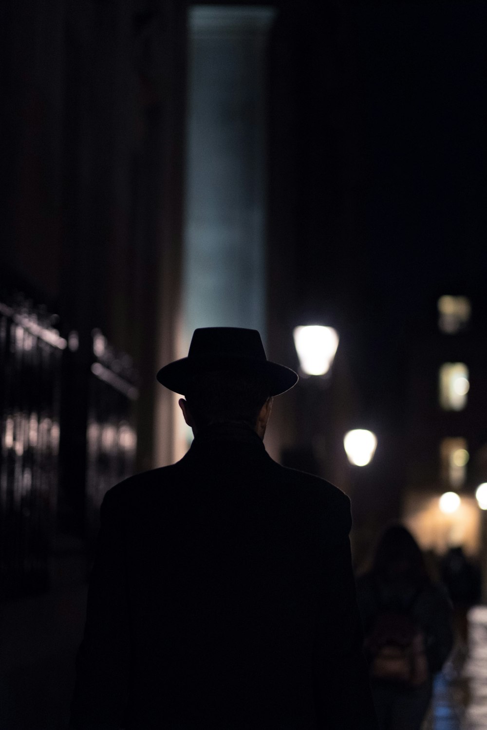 검은 모자를 쓴 남자가 밤에 보도를 걷고 있습니다.