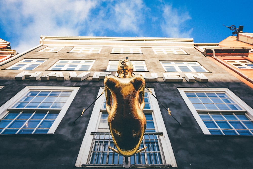 Flachwinkelfotografie der braunen Frauenstatue vor dem Gebäude unter weißem und blauem Gebäude