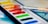 A watercolor paint set is shown with various colors including yellow, green, red, and blue. A paintbrush with red paint on its bristles is resting on top of the palette.