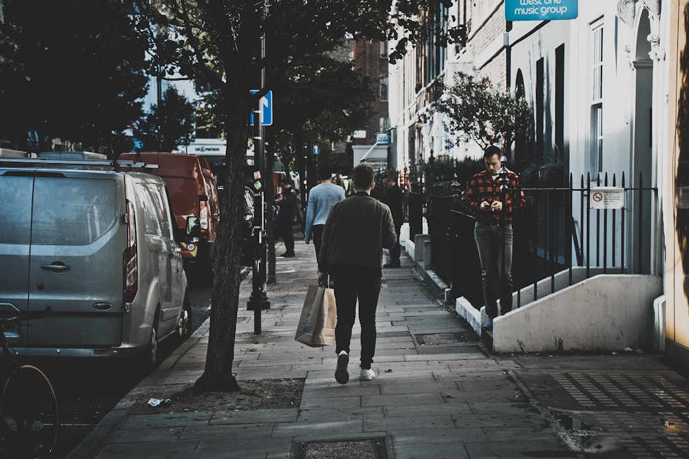 hombre que camina por la calle al lado de los edificios mientras sostiene una bolsa de papel