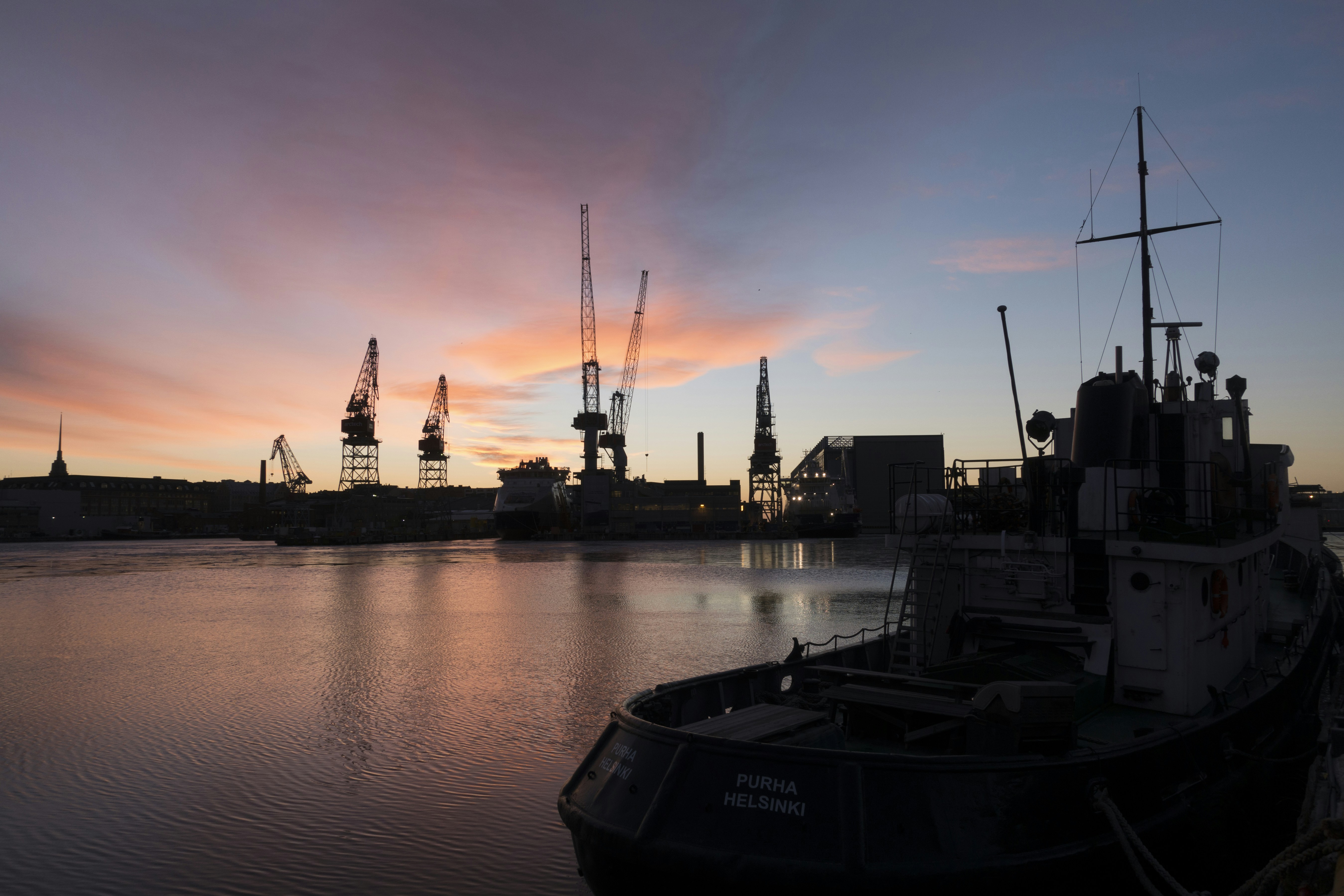 Sunset glow illuminating a docked cargo ship with cranes silhouetted against the sky.