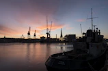 A busy dockyard with cranes loading marine equipment onto a ship at sunset.