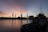 A harbor scene at sunset with several large cranes silhouetted against a colorful sky. A ship is moored in the foreground, set against the backdrop of the industrial dock area.