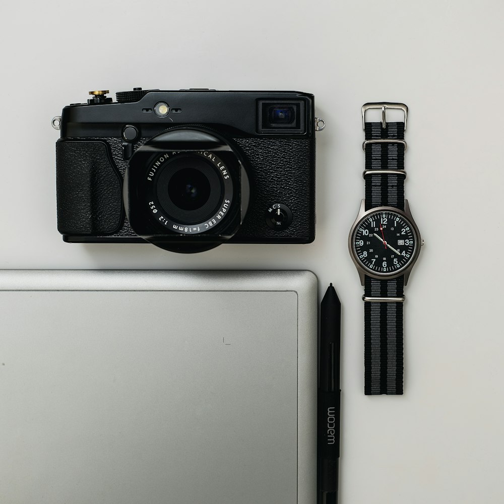 Fotocamera point-and-shoot nera e orologio analogico rotondo nero con cinturino in tessuto
