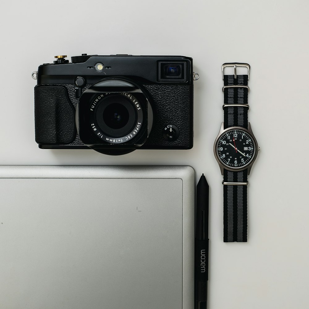 black point-and-shoot camera and round black analog watch with fabric band