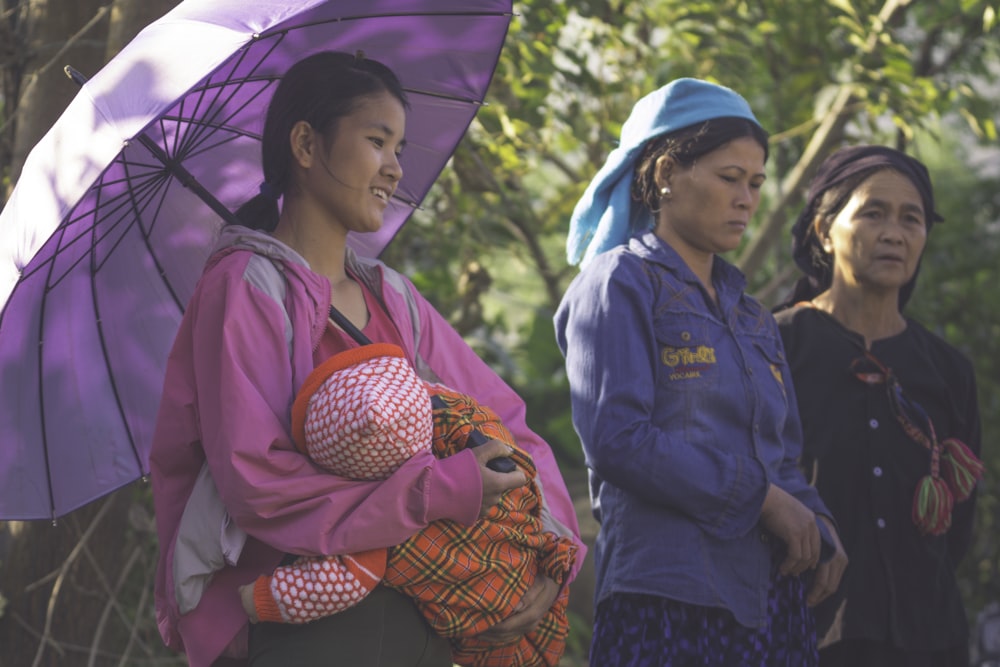 woman carrying baby under purple umbrella