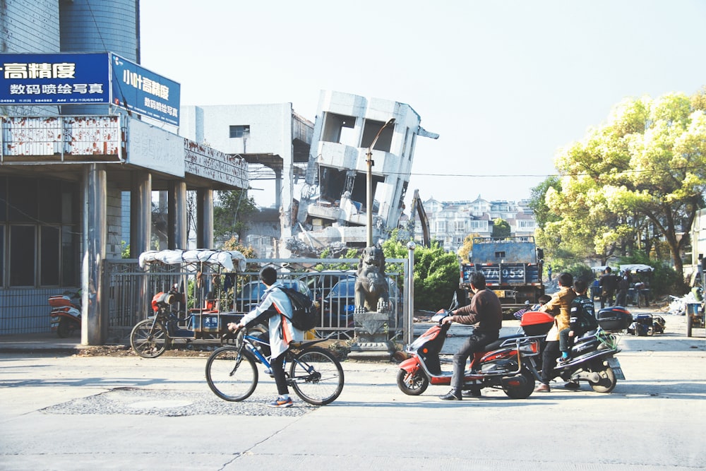 three men riding bicycle and motor scooters near building at daytime