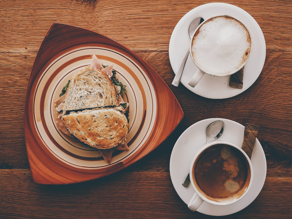 sandwich al prosciutto sul piatto vicino al cappuccino sulla tazza e caffè