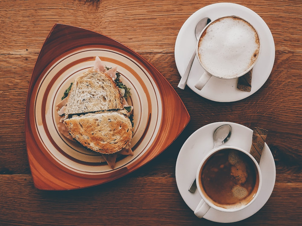 Sándwich de jamón en el plato cerca del capuchino en la taza y el café