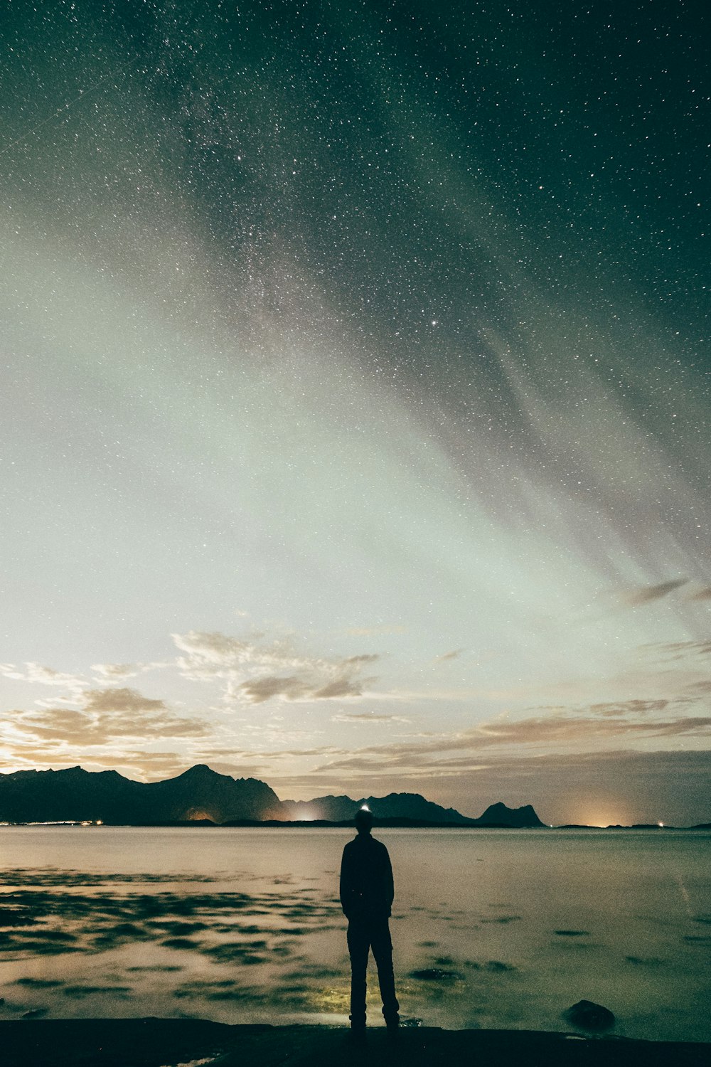 silhouette of man facing body of water under white clouds at golden hour