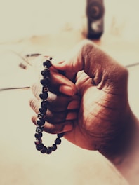 A hand holding a beaded bracelet with letters spelling 'BLACK' against a blurred background. The skin tone is rich and smooth, and the focus on the hand and bracelet creates an intimate and detailed view.