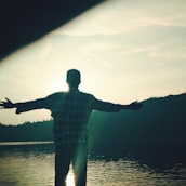 Serene outdoor scene with a person stretching by a calm lake at sunrise.