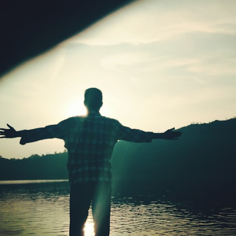 A serene outdoor scene of a man stretching at sunrise by a lake.