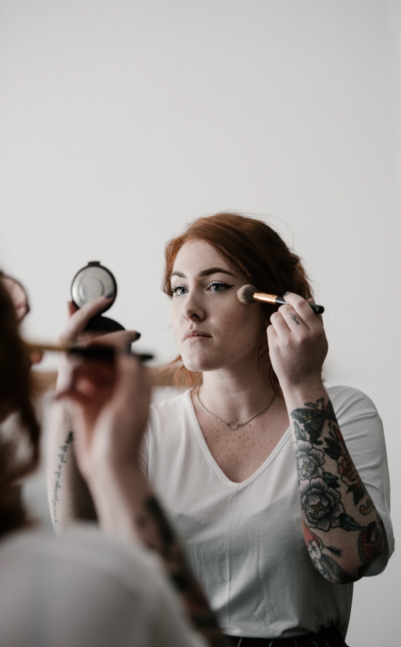 Woman applying facial makeup with a beauty brush in front of a mirror