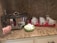 A kitchen countertop with a large slow cooker, a container of candy canes, a small green bowl of marshmallows, and a red tray holding nine white mugs with whimsical designs. The countertop is made of granite with a speckled pattern.