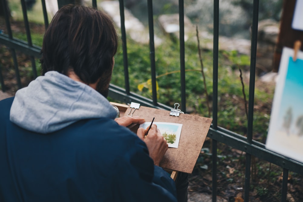 man drawing on paper beside fence