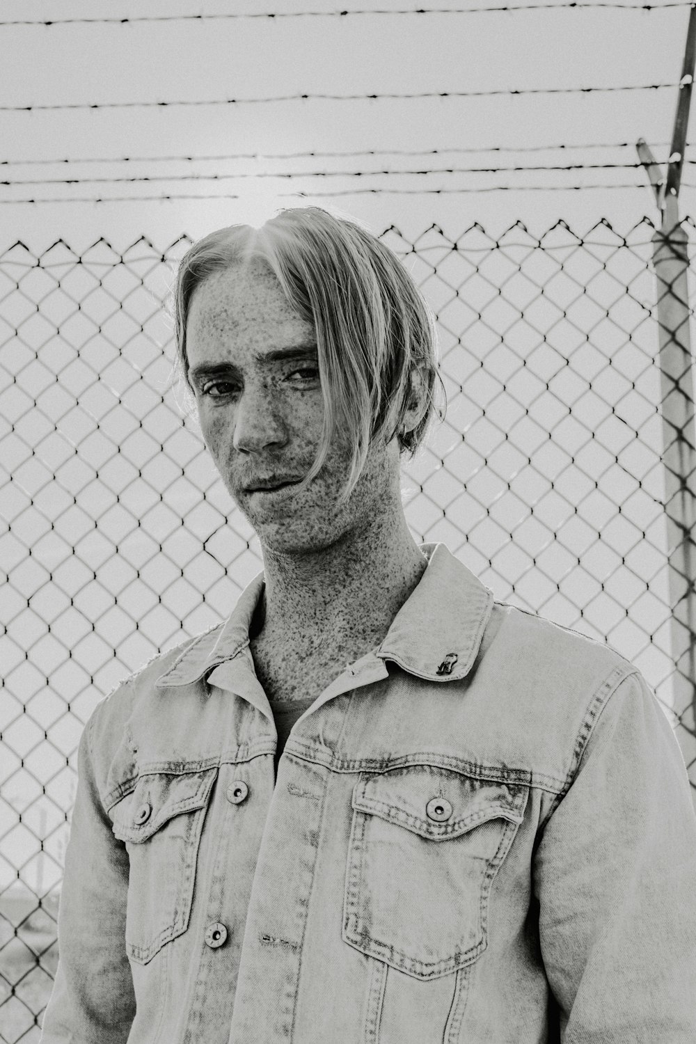 grayscale photography man standing beside fence