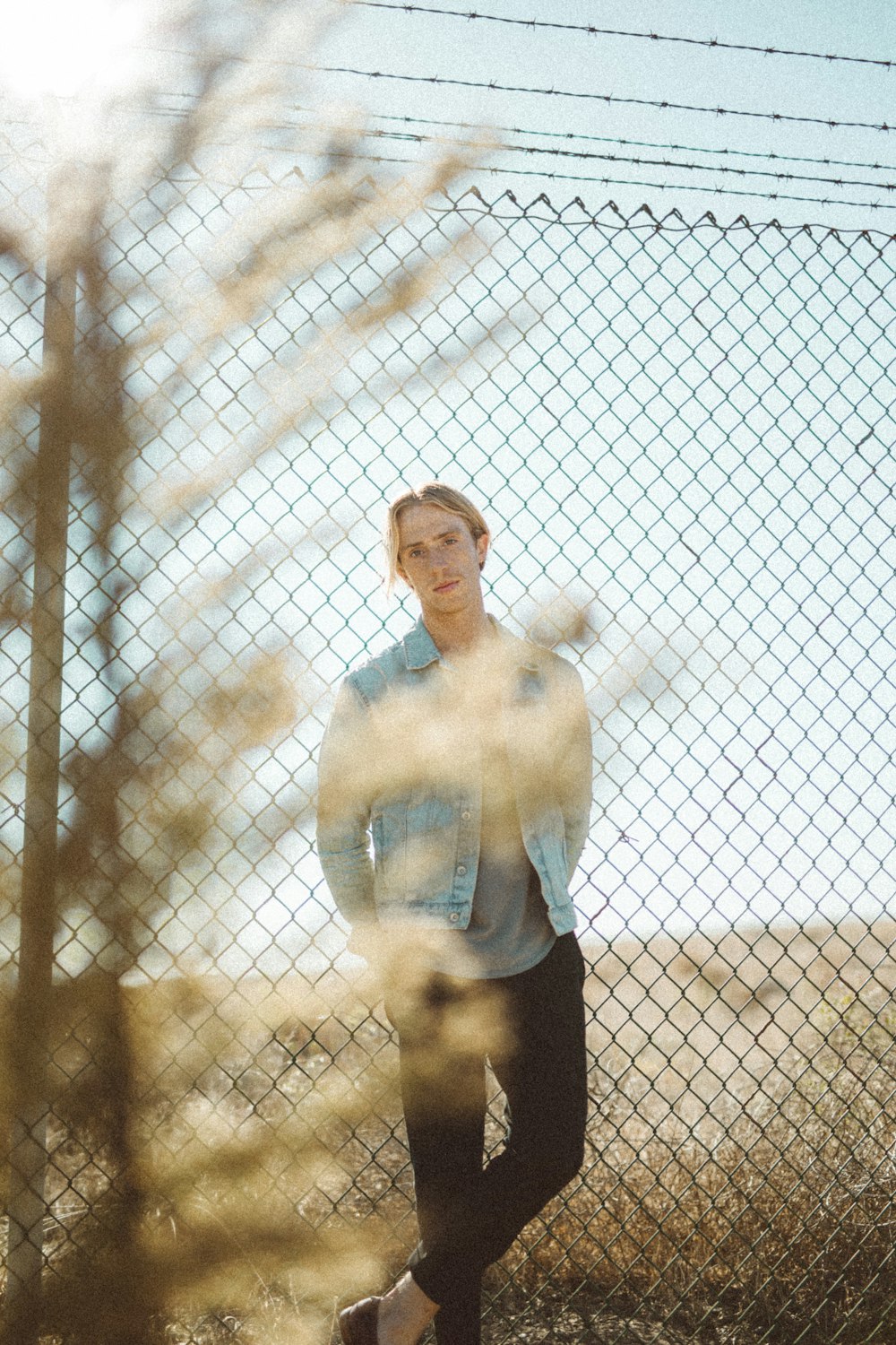 man wearing blue denim jacket beside chain link fence