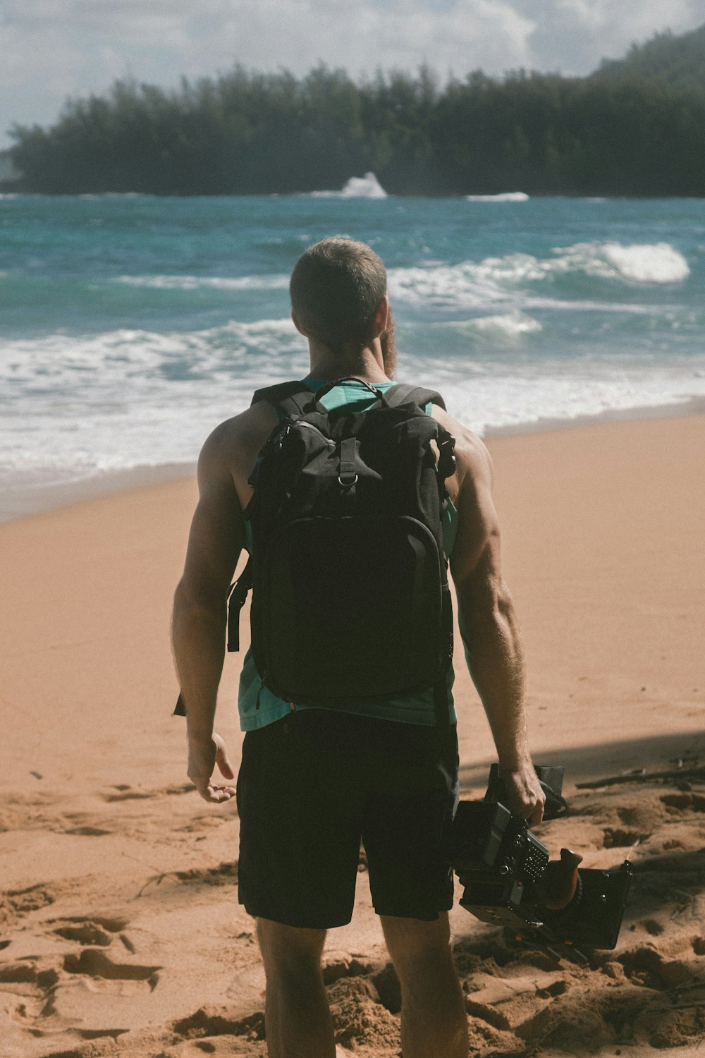 man carrying video camera standing on beach sand facing sea