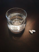 A variety of headache relief tablets with a glass of water on a bedside table.