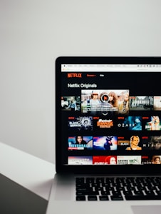 A laptop displaying the Netflix Originals section with various show thumbnails, including Stranger Things, Black Mirror, and Riverdale. The screen interface includes a list of shows available for viewing.