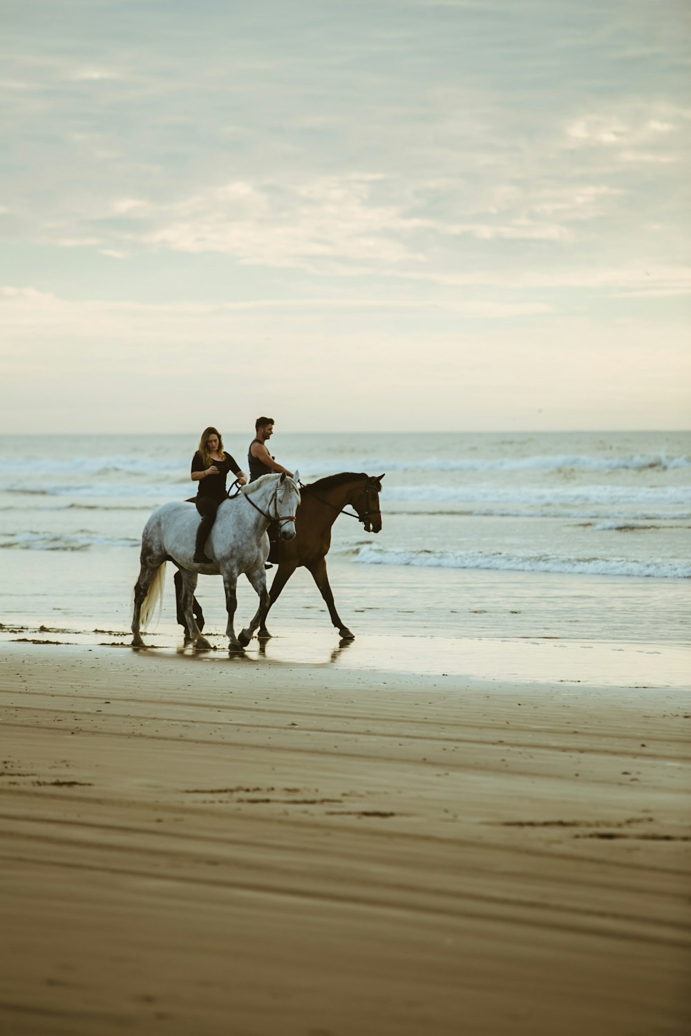 Man en vrouw aan het paardrijden langs de kust