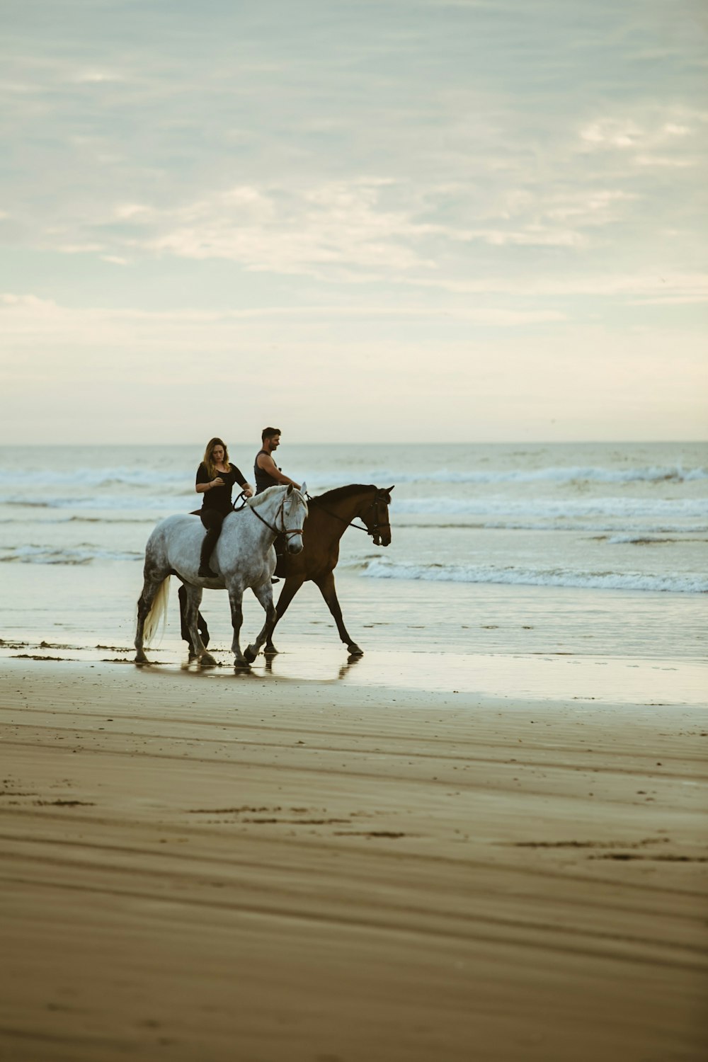 man and woman riding on horse near seashore