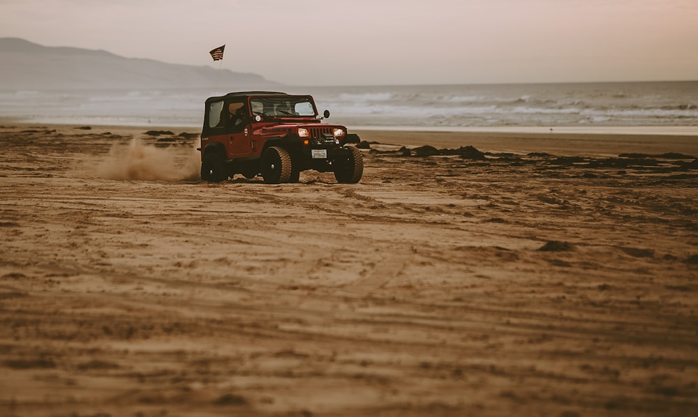 roter Jeep Wrangler am Meeresufer in der Nähe eines Gewässers bei Tag