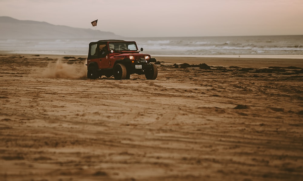 red Jeep Wrangler on seashore near body of water at daytime