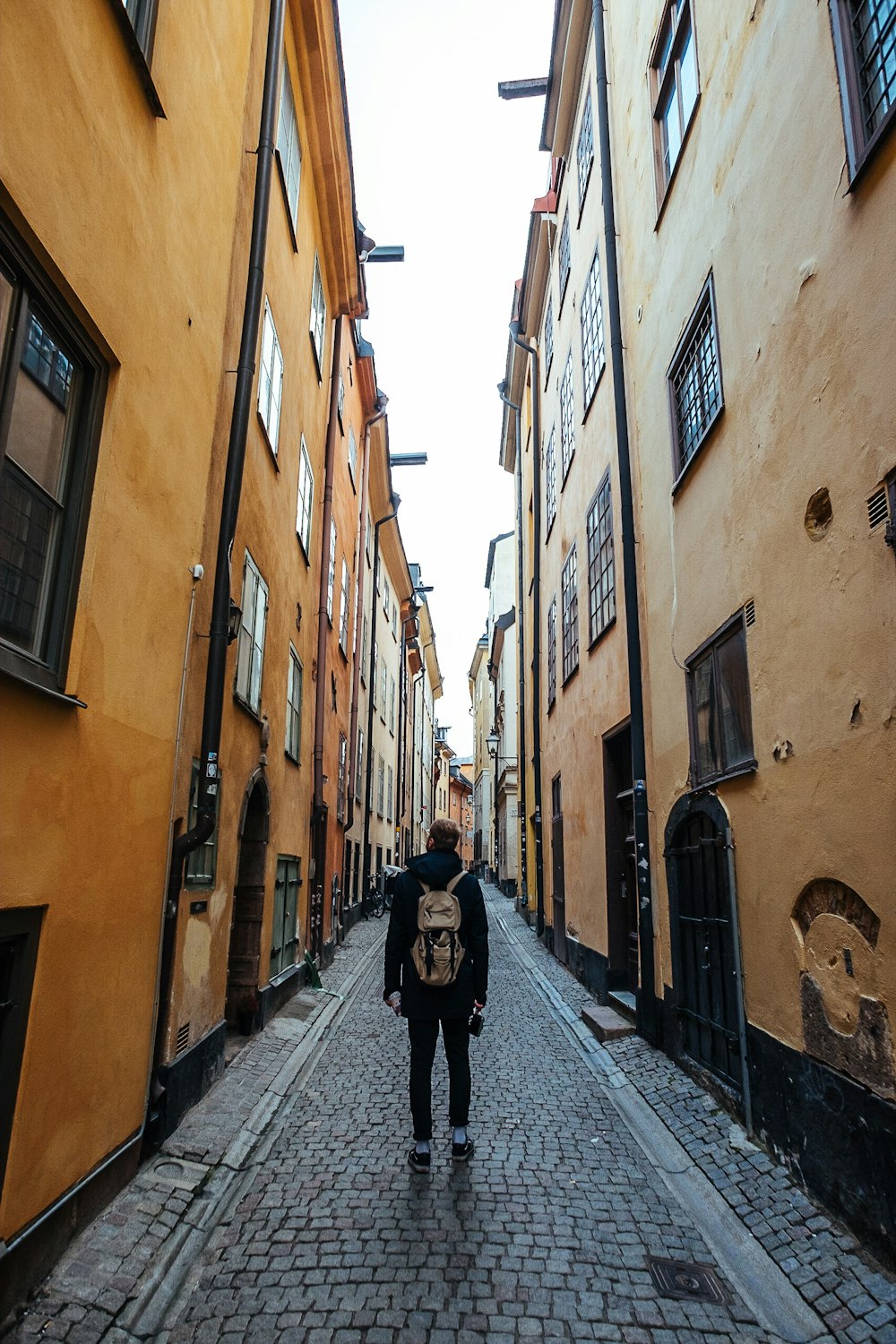 Mann in schwarzem langärmeligem Oberteil und braunem Rucksack geht auf der Straße