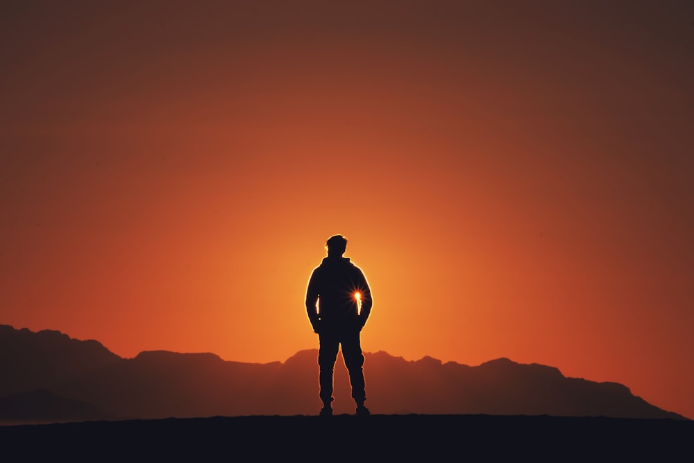 silhouette photography of person standing on platform with mountain background during golden hour