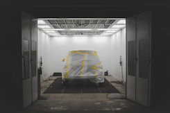 Close-up of a freshly sprayed black bedliner coating on a pickup truck bed under bright yellow workshop lights.