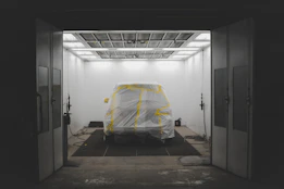 Close-up of a freshly sprayed black bedliner coating on a pickup truck bed under bright yellow workshop lights.